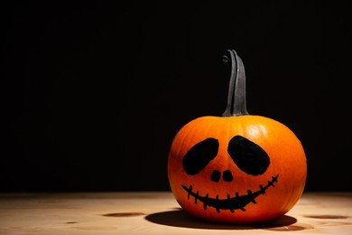 Halloween celebration. Pumpkin with drawn face on wooden table against black background, space for text