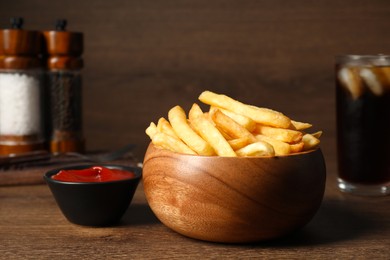 Delicious fresh french fries in bowl and tomato sauce on wooden table, closeup