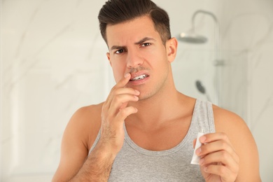 Photo of Emotional man with herpes applying cream on lips in bathroom