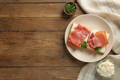 Photo of Delicious sandwiches with cream cheese and jamon on wooden table, flat lay. Space for text
