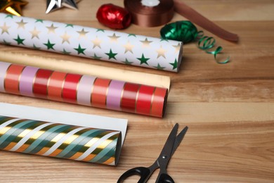 Photo of Colorful wrapping paper rolls, scissors and ribbons on wooden table