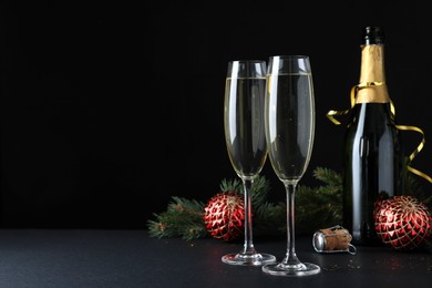 Happy New Year! Bottle of sparkling wine, glasses and festive decor on table against black background, space for text