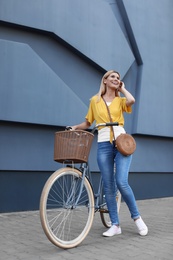 Woman with bicycle on street near gray wall