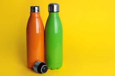 Stylish stainless thermo bottles on yellow background. Space for text