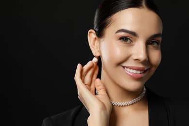 Young woman with elegant pearl jewelry on black background, closeup. Space for text