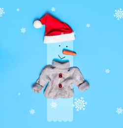 Snowman with Santa hat and small sweater on light blue background, flat lay