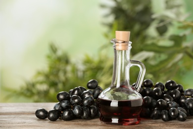Glass jug with wine vinegar and fresh grapes on wooden table against blurred background