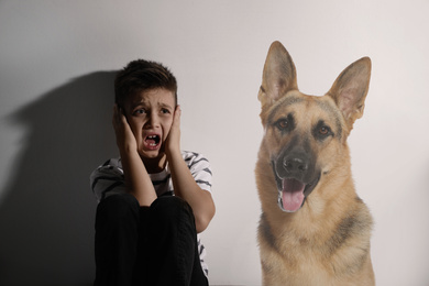 Scared little boy suffering from cynophobia on white background. Irrational fear of dogs