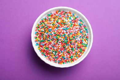 Colorful sprinkles in bowl on purple background, top view. Confectionery decor