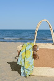 Straw bag with beach wrap and sunglasses on sandy seashore. Summer accessories