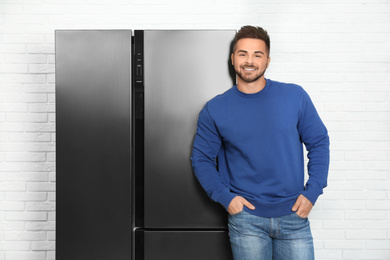 Happy young man near modern refrigerator indoors