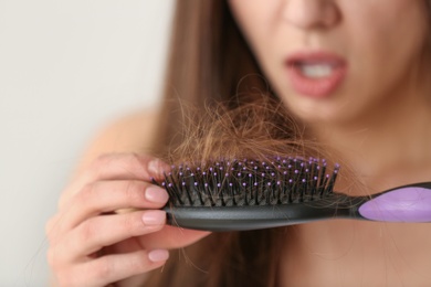Photo of Woman untangling her hair from brush on light background, closeup