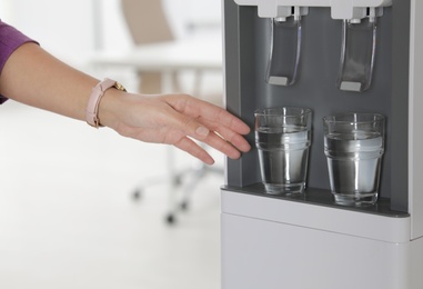 Woman taking glass of water from cooler in office, closeup