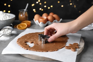 Photo of Woman making Christmas gingerbread man cookies at light grey table, closeup