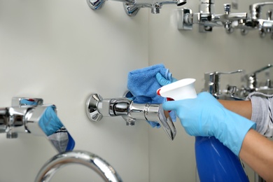 Woman cleaning faucets with rag and detergent in bathroom fixtures store, closeup