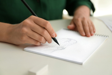 Woman drawing with pencil in notepad at white table, closeup