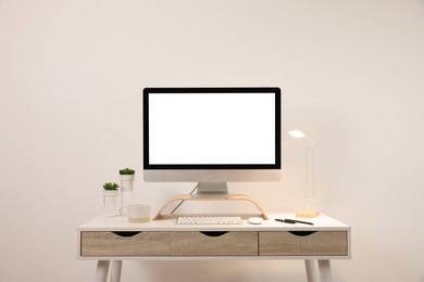 Comfortable workplace with blank computer display on desk near light wall. Space for text