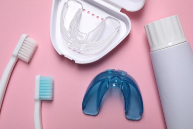 Photo of Bite correction. Toothpaste, brushes and dental mouth guards on pink background, flat lay