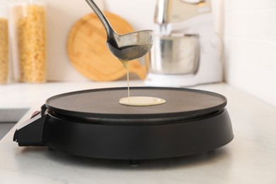Cooking delicious crepe on electric pancake maker in kitchen, closeup