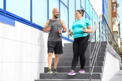 Overweight man and woman running with dumbbells on stairs outdoors