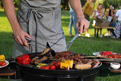 Man cooking meat and vegetables on barbecue grill in park, closeup