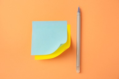 Photo of Blank paper notes and pen on pale orange background, flat lay