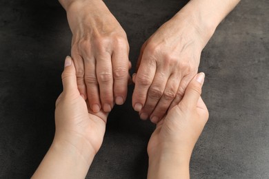 Young and elderly women holding hands at dark grey table, closeup