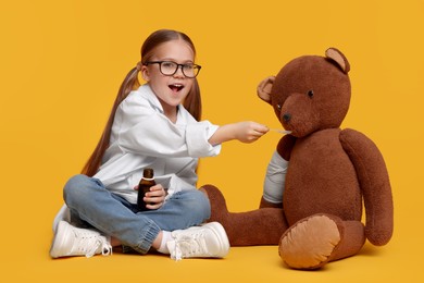 Photo of Little girl playing doctor with toy bear on yellow background