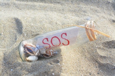 Glass bottle with seashells and message SOS on sand, closeup