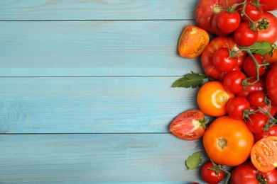 Many different ripe tomatoes on light blue wooden table, flat lay. Space for text