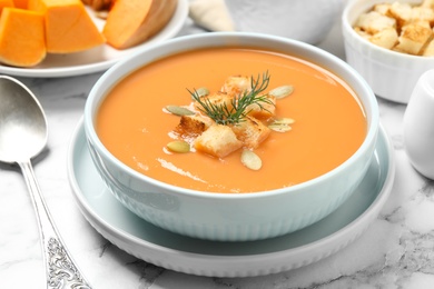 Tasty creamy pumpkin soup with croutons, seeds and dill in bowl on white marble table