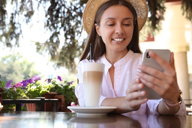 Beautiful young woman with coffee and smartphone at table in outdoor cafe