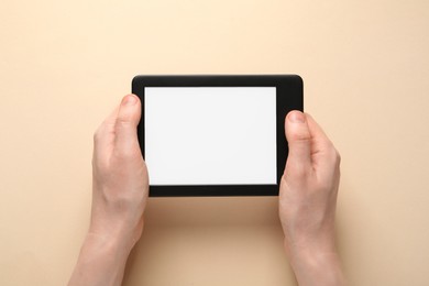 Woman using e-book reader on beige background, top view