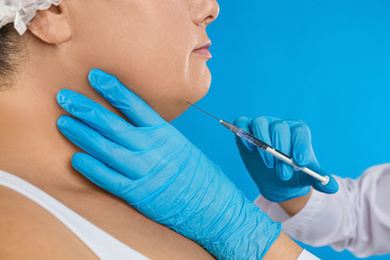 Woman with double chin getting injection on blue background, closeup. Cosmetic surgery