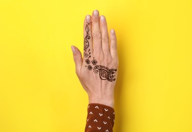Woman with henna tattoo on hand against yellow background, closeup. Traditional mehndi ornament