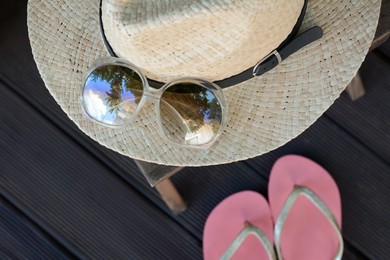 Stylish hat with sunglasses and flip flops on wooden floor, top view. Beach accessories