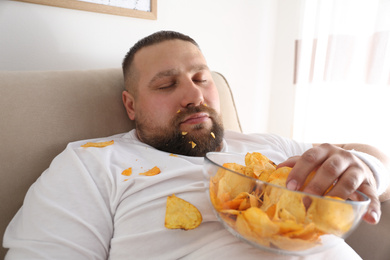 Lazy overweight man with chips sleeping on sofa at home, closeup