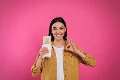 Photo of Happy young woman with delicious shawarma on pink background