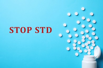 Bottle with pills and text STOP STD on light blue background, flat lay