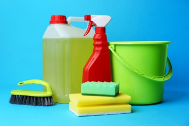 Green bucket, cleaning supplies and tools on light blue background