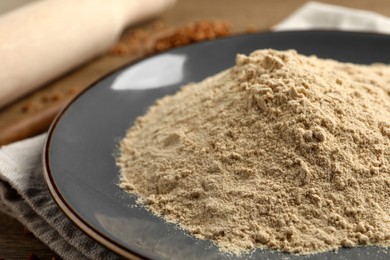 Plate with buckwheat flour on wooden table, closeup
