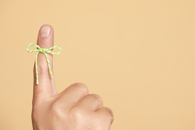 Man showing index finger with tied bow as reminder on beige background, closeup. Space for text