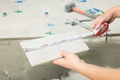 Worker measuring tile near adhesive mix on floor, closeup