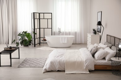 Stylish light apartment interior with white bathtub and bed