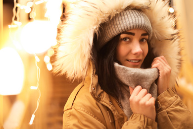 Beautiful young woman near festive lights outdoors. Winter vacation