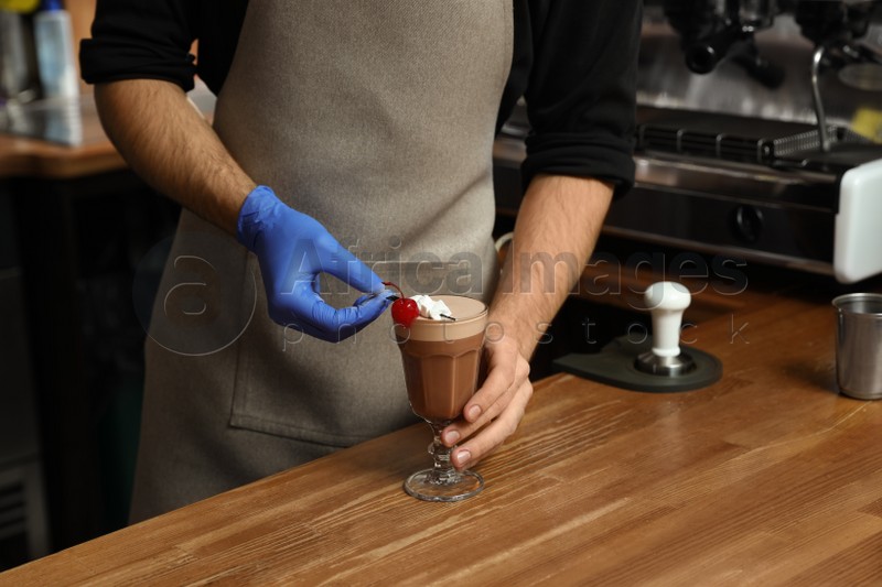 Barista decorating glass of coffee drink on bar counter, closeup