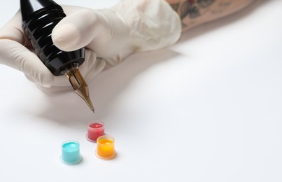 Tattoo artist with professional machine and colorful ink on white background, closeup