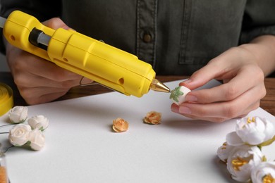 Photo of Woman with hot glue gun making craft at white wooden table, closeup