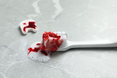 Photo of Decorative tooth and toothbrush with blood on light grey marble table, closeup. Gum inflammation