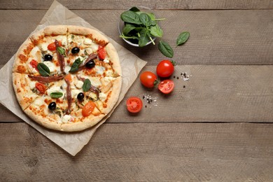 Photo of Tasty pizza with anchovies and ingredients on wooden table, flat lay. Space for text